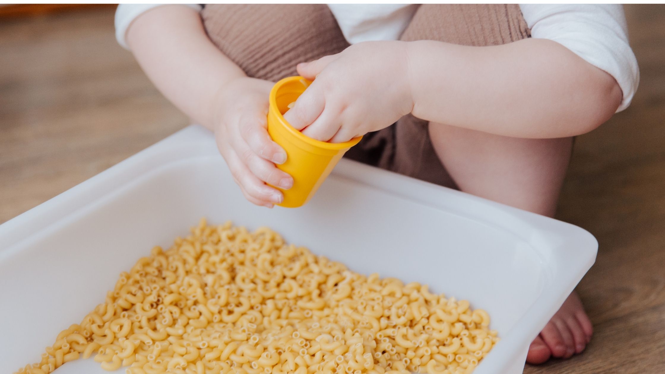 A picture of a toddler playing with pasta in a busybox.